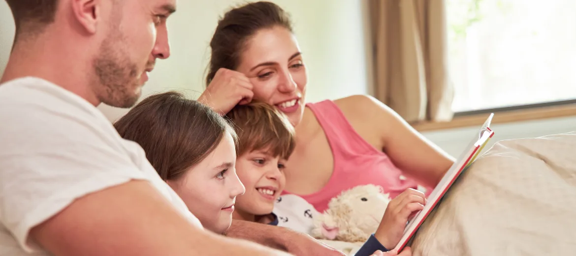 25-08-Vorlesen-sikjm-kiga-1-schweizer-elternmagazin-hg Vorlesen: Eltern mit zwei Kinder lesen im Bett eine Geschichte vor