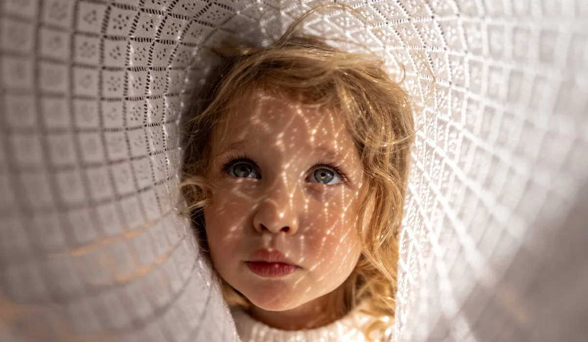 Hypnose bei Kindern: Ein Mädchen schaut durch einen weissen Stoff