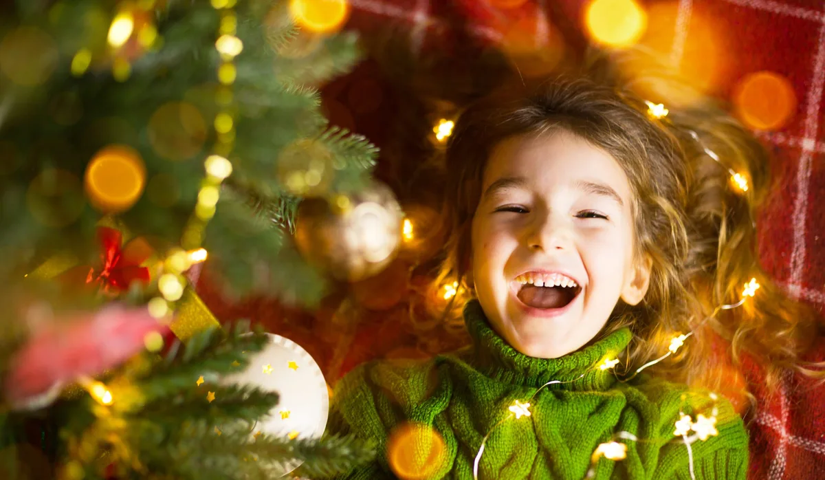 Weihnachten, die Geschichte von der Weihnachtsspinne: Ein Mädchen liegt strahlend neben einem Christbaum