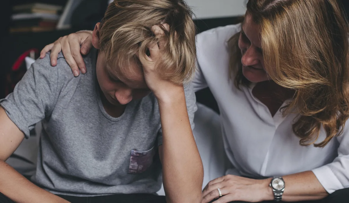 Mother consoling her upset son Angst: Eine Mutter sitzt neben ihrem Teenager-Sohn und legt den Arm auf seine Schulter