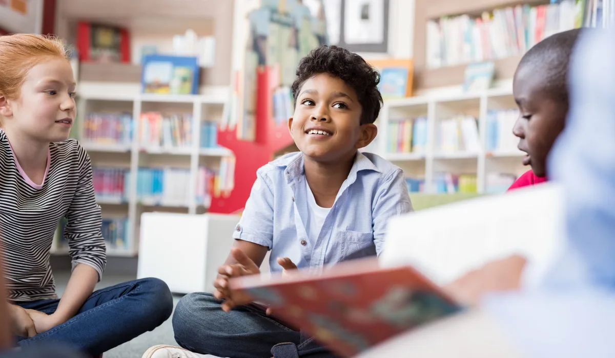 Lesen: Drei Kinder im Primarschulter hören aufmerksam einer Geschichte zu