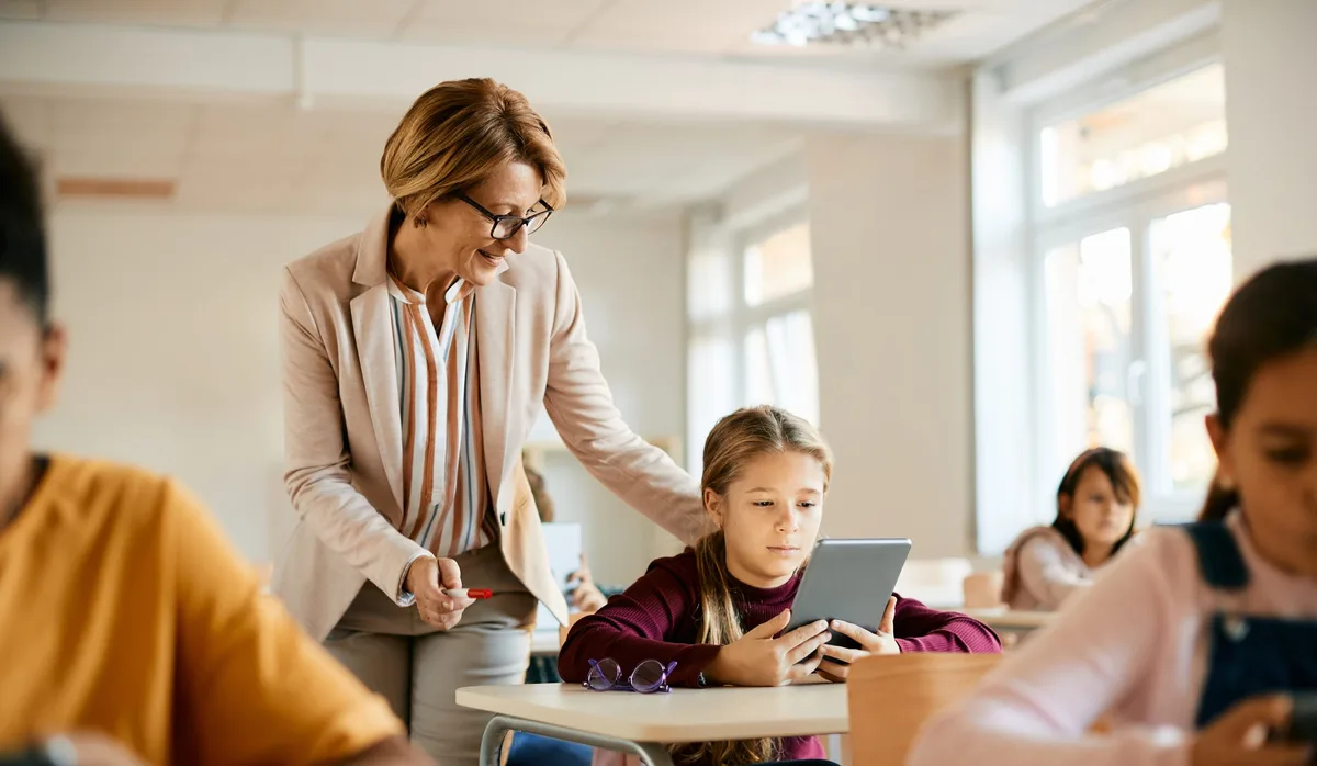 Senior teacher assists schoolgirl in using digital tablet during a class at school. Lehrerin im Klassenzimmer