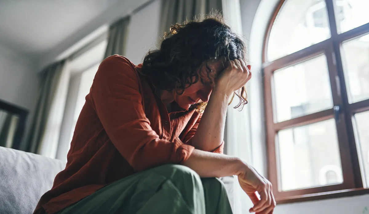 Distressed Woman Sitting on a Sofa in a Sunny Apartment Verzweifelte Frau sitzt auf dem Bett