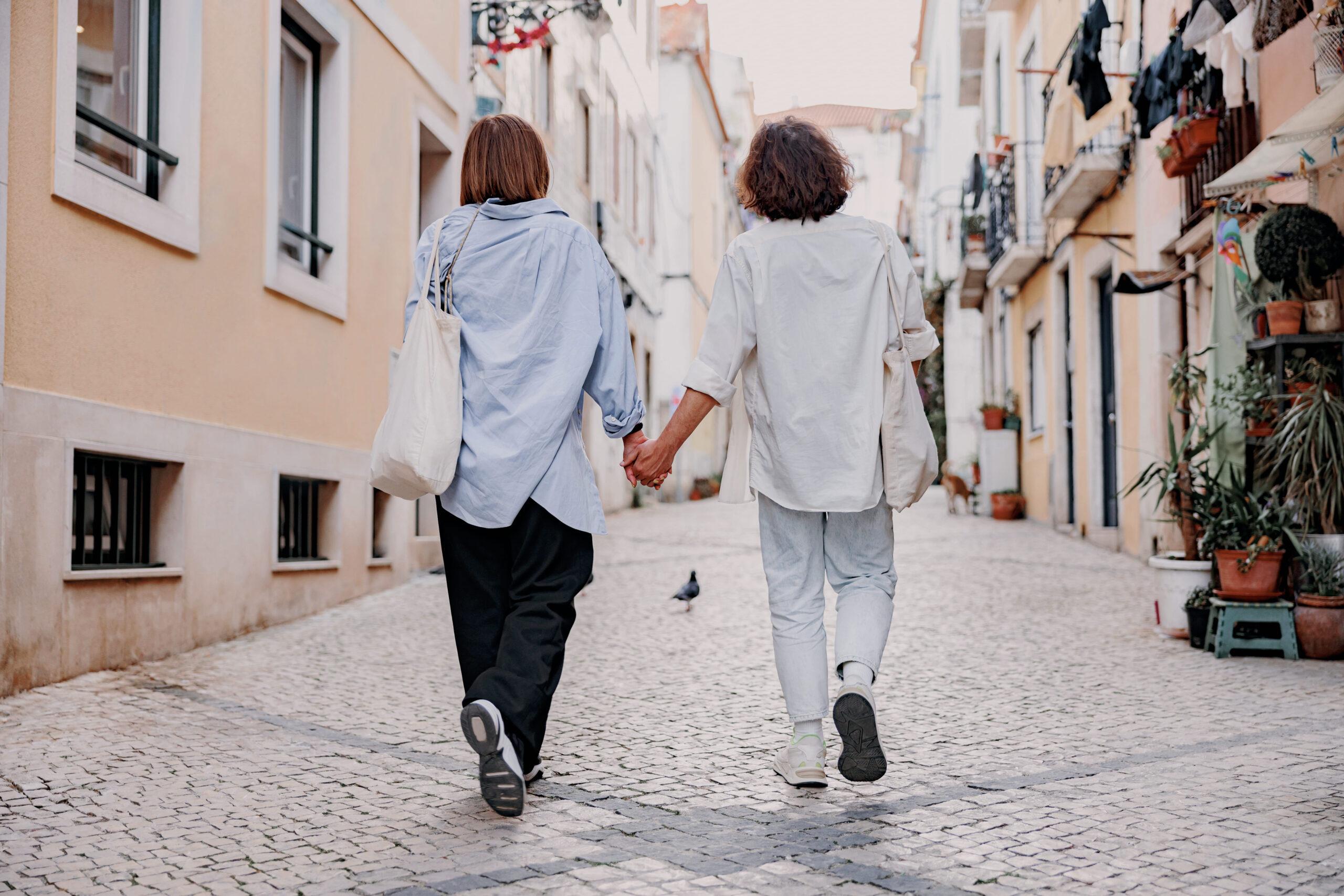 Back view of tourist couple hugging and walking on Lisbon street, enjoying sightseeing outdoors