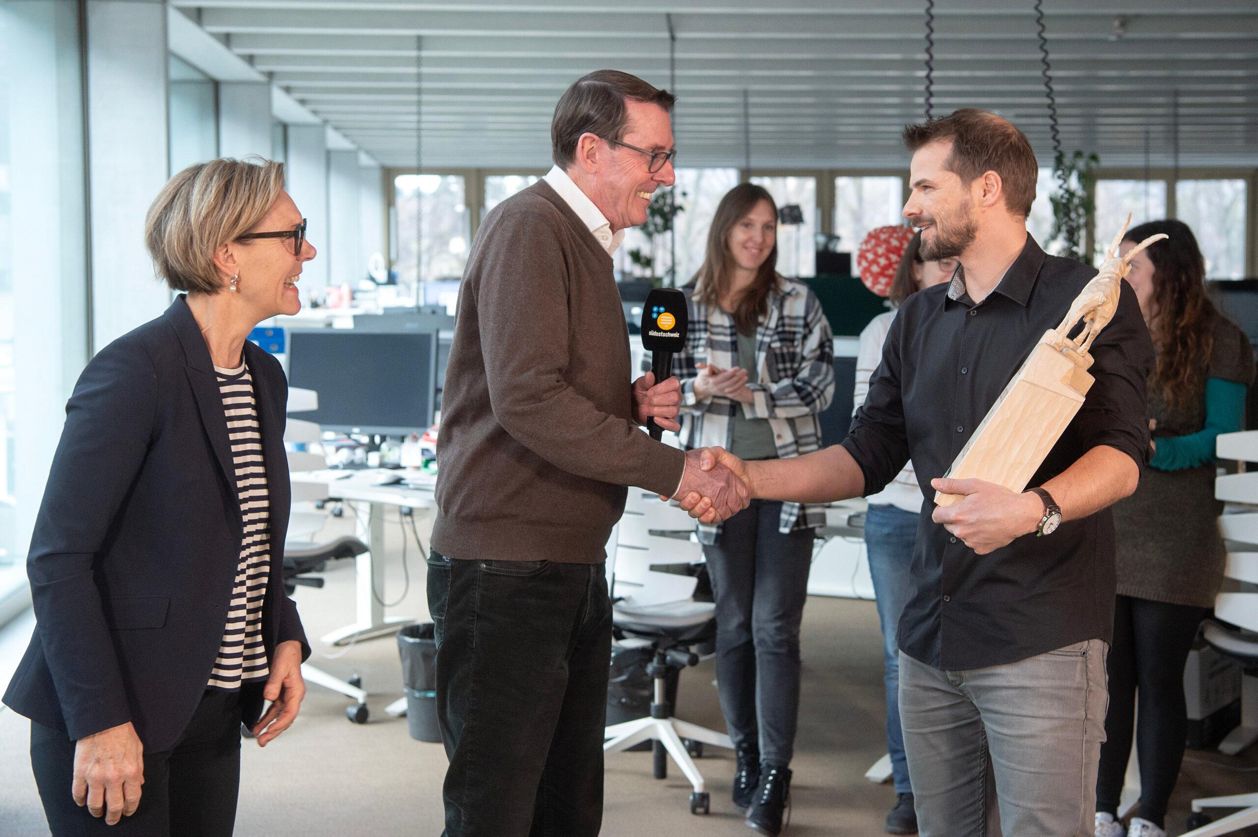 Christian Loretz (rechts) bekommt die Steinbocktrophäe von den Vorjahressiegern Claudia und Andreas Züllig im Medienhaus Somedia in Chur überreicht. 