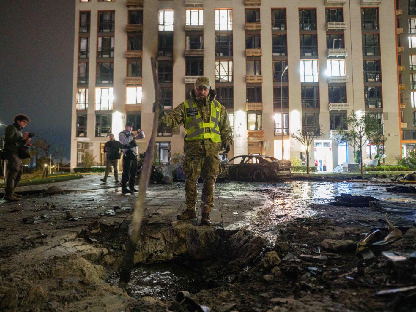 Ein Polizeibeamter sucht vor einem mehrstöckigen Wohnhaus in Kiew, das bei einem russischen Drohnenangriff beschädigt wurde, nach Trümmern einer Drohne. Foto: Evgeniy Maloletka/AP/dpa