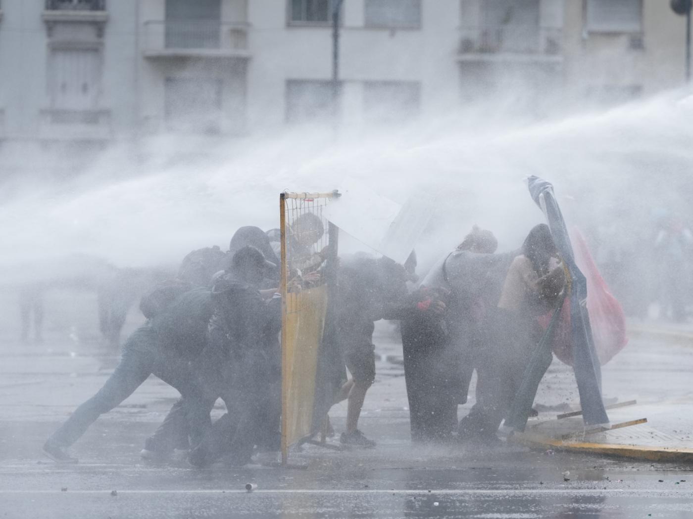 dpatopbilder - Demonstranten suchen Deckung, während die Polizei bei einer regierungskritischen Demonstration einen Wasserwerfer einsetzt, um sie auseinanderzutreiben. Foto: Rodrigo Abd/AP/dpa