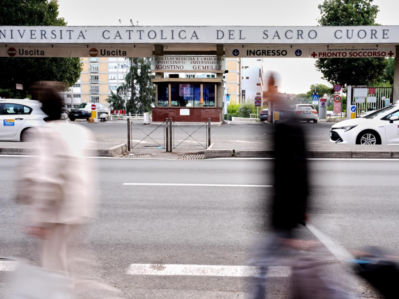 Passanten gehen am Haupteingang der Poliklinik "Agostino Gemelli" vorbei, in der Papst Leo XIV. in den nächsten Tagen zur Entfernung eines Lungenknotens stationär aufgenommen werden soll. Foto: Andrew Medichini/AP/dpa