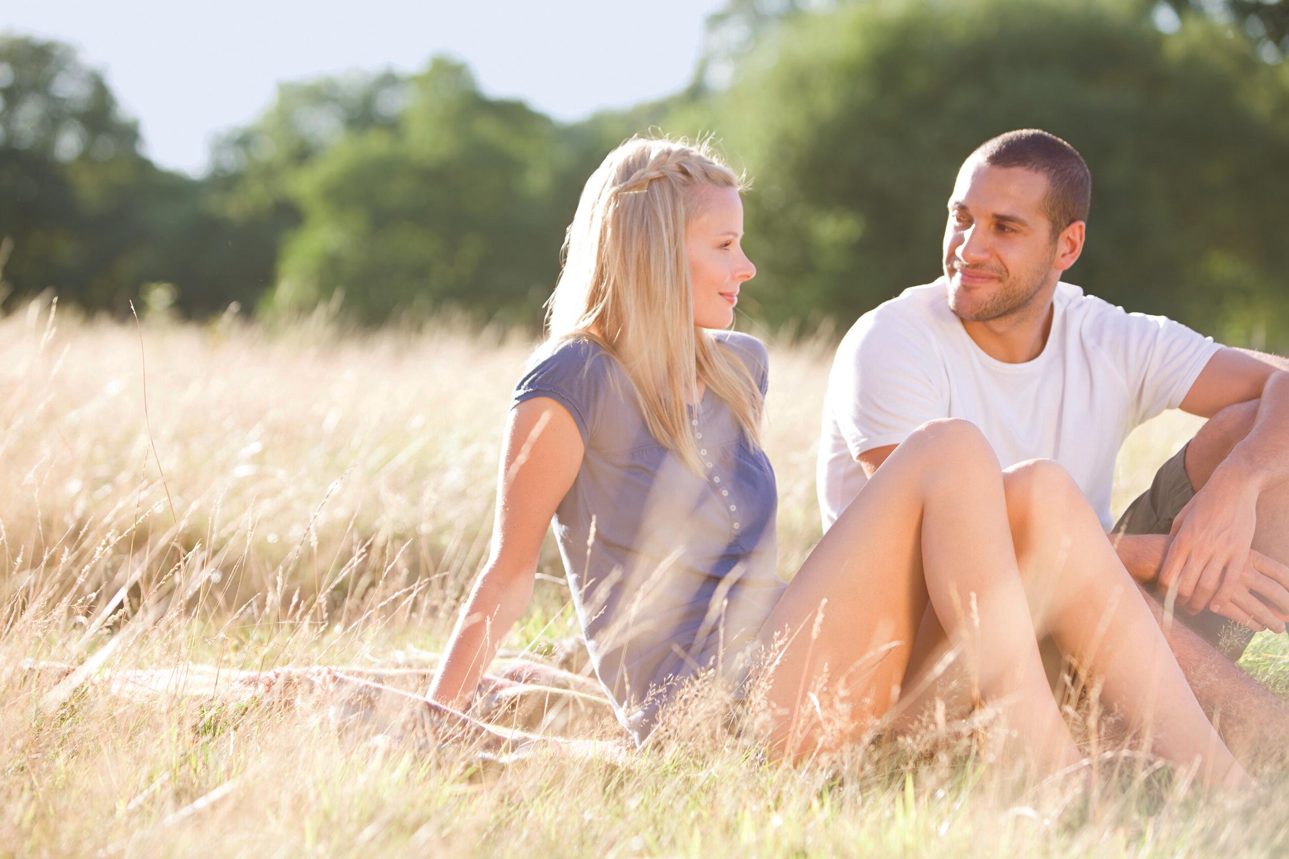 A young couple sitting on the grass in summertime, smiling