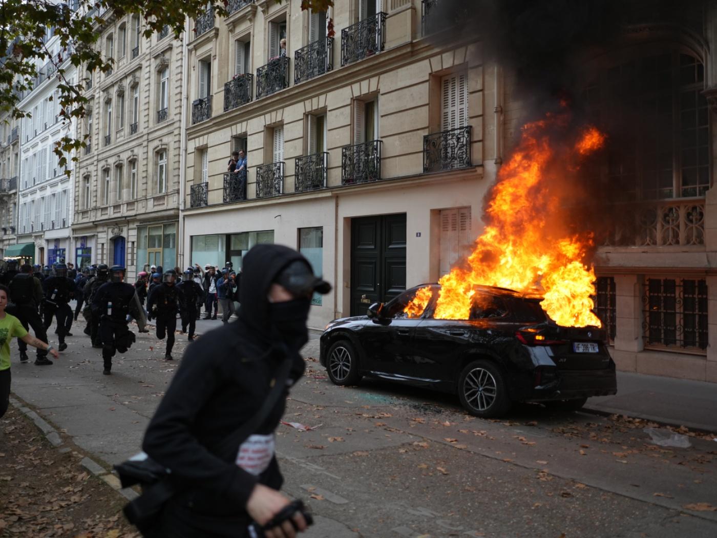 dpatopbilder - Ein Demonstrant läuft während eines Marsches gegen unterfinanzierte Schulen an einem brennenden Auto vorbei. Foto: Thibault Camus/AP/dpa