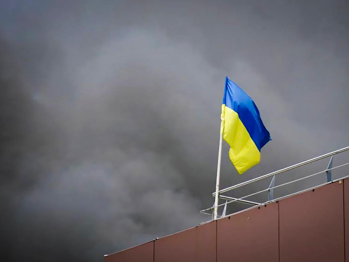 HANDOUT - Eine ukrainische Flagge weht, während im Hintergrund nach einem russischen Angriff Rauch aufsteigt. Foto: Uncredited/Dnipro Regional Administration/AP/dpa/Symbolbild