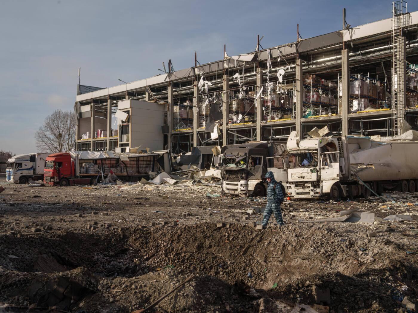 ARCHIV - Ein Wachmann betrachtet einen Krater vor einem Novus-Logistikzentrum, das bei einem russischen Angriff auf Kiew beschädigt wurde. Foto: Evgeniy Maloletka/AP/dpa (Archivbild)