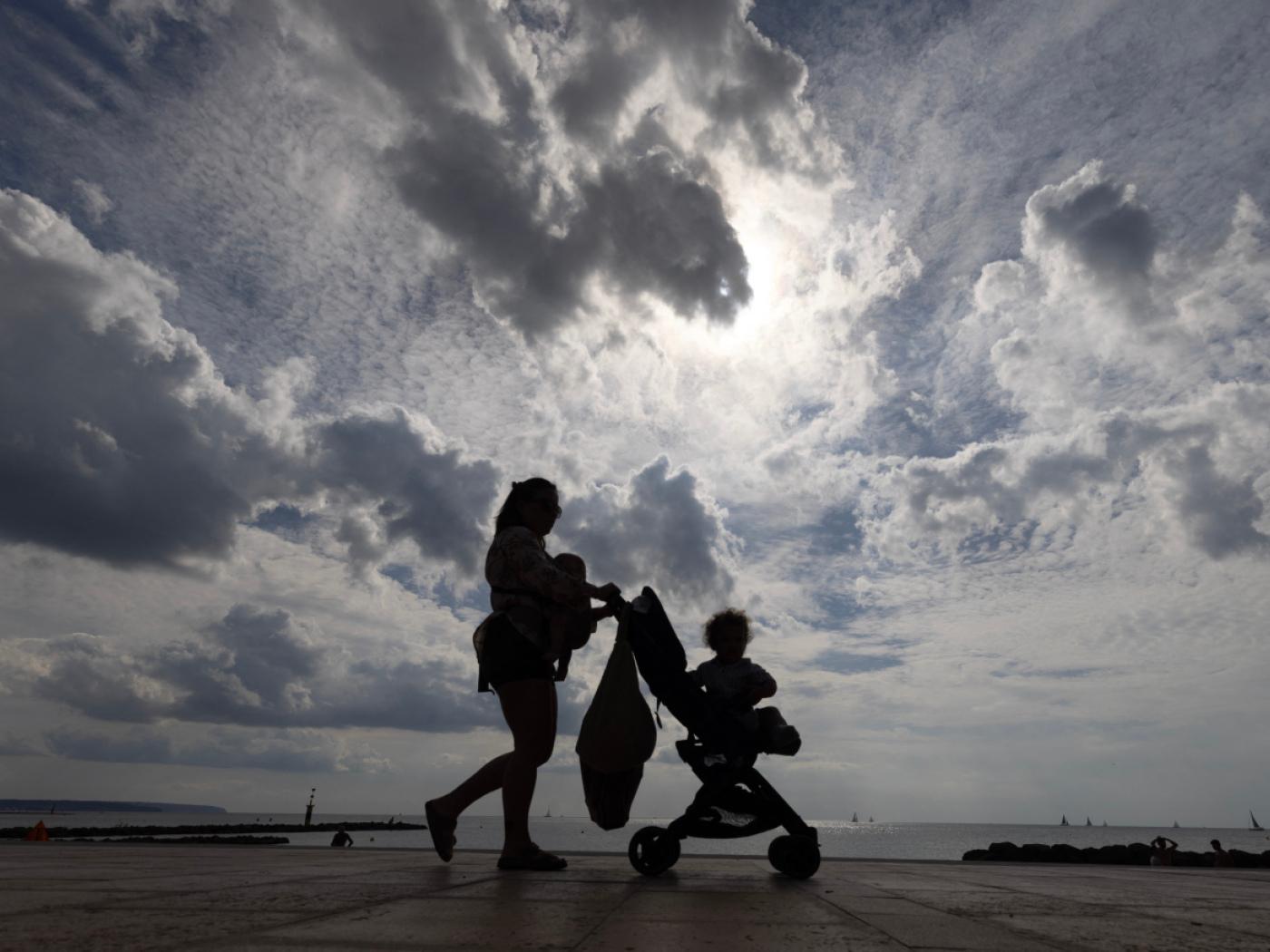Eine Frau spaziert mit ihrem Kinderwagen am Strand Ciudad JardÌn auf Mallorca entlang. Foto: Clara Margais/dpa/Symbolbild