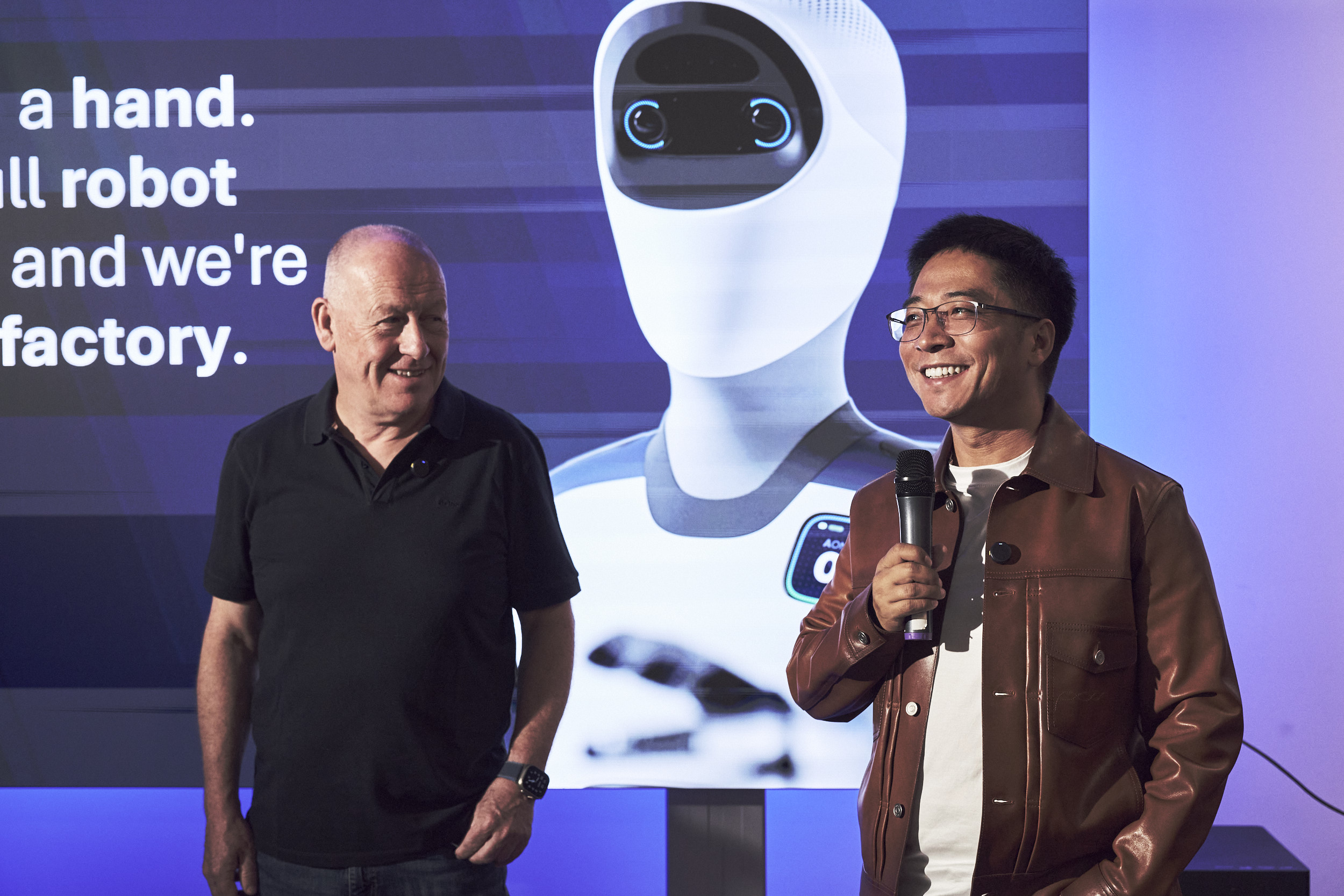 Agile-Robots-Gründer Zhaopeng Chen (re.) und Rory Sexton (Executive Director) vor dem Bild eines Humanoiden Roboters