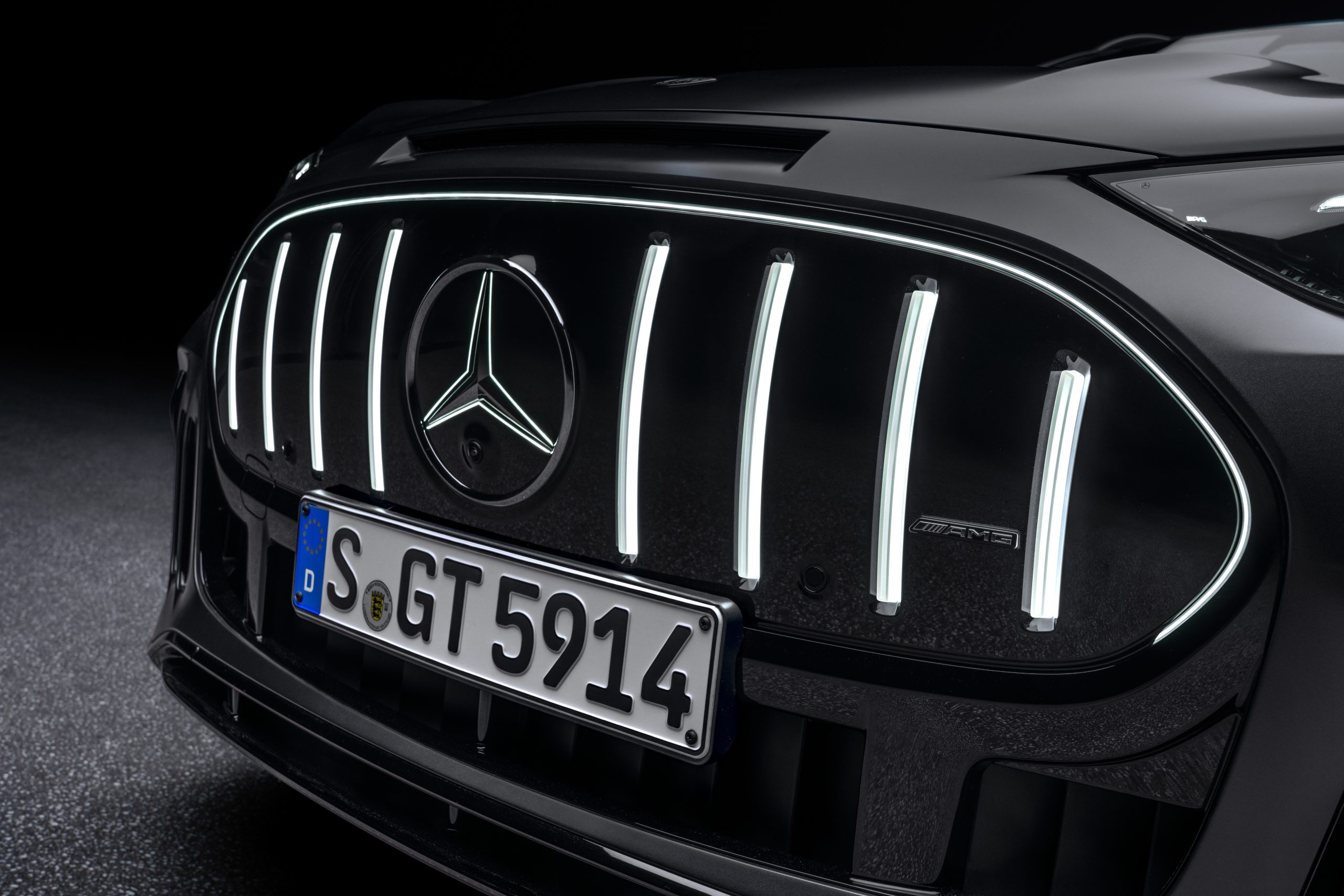 Nahaufnahme des beleuchteten Frontgrills am schwarzen Mercedes-AMG GT SUV mit vertikalen LED-Leuchtstreben und Mercedes-Stern. 