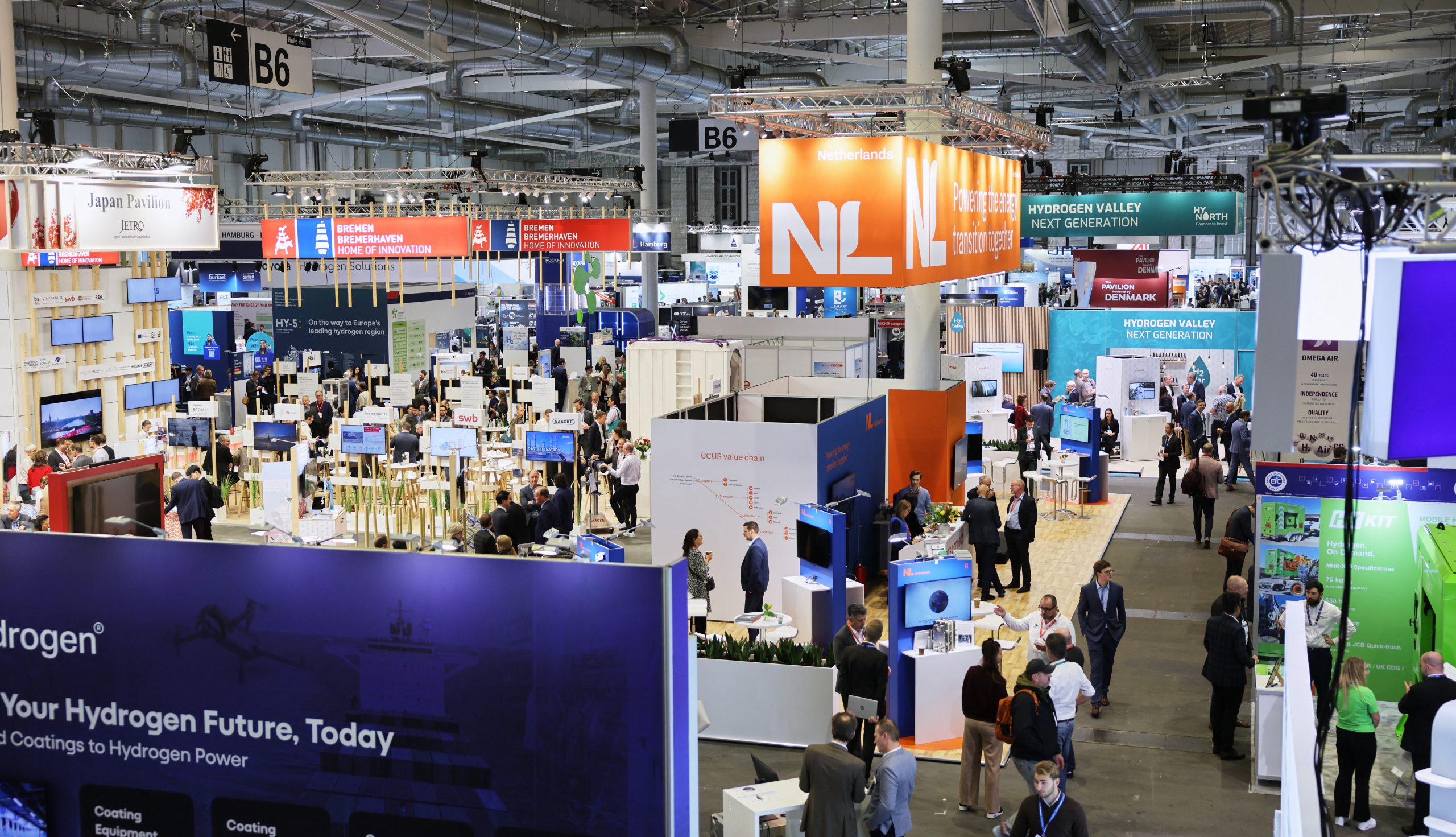 Blick von oben in eine Messehalle der Hydrogen Technology Expo 2026 in Hamburg mit zahlreichen Ständen, Länderpavillons der Niederlande, Dänemarks und Japans sowie Besuchern in den Gängen.