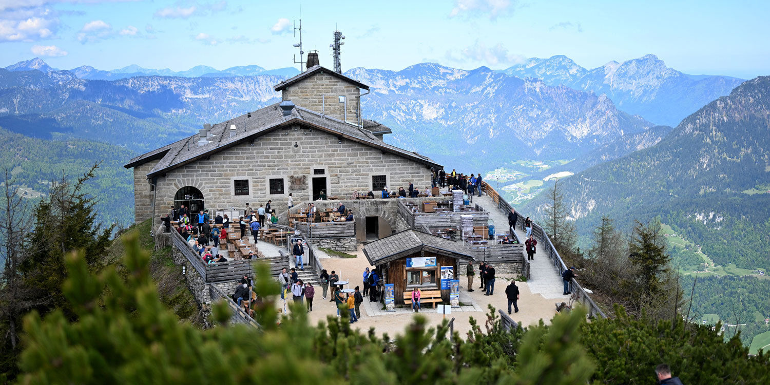 Kehlsteinhaus aus hellem Naturstein mit großer Aussichtsterrasse und zahlreichen Besuchern, im Hintergrund die Gipfel der Berchtesgadener Alpen.