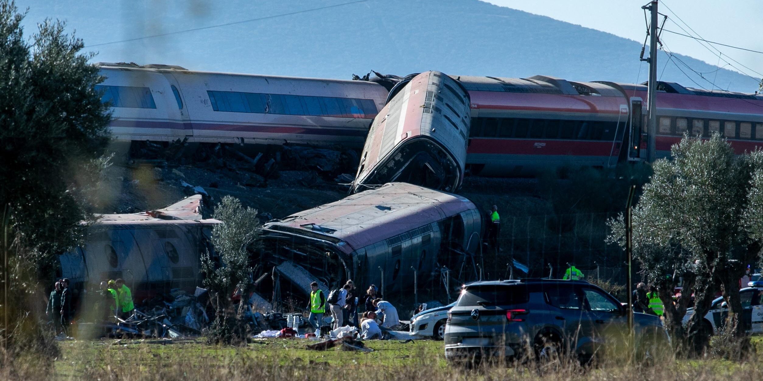 Schwer beschädigte und entgleiste Hochgeschwindigkeitszüge in Spanien. Mehrere Waggons liegen übereinander und neben den Gleisen, während Rettungskräfte an der Unfallstelle arbeiten.