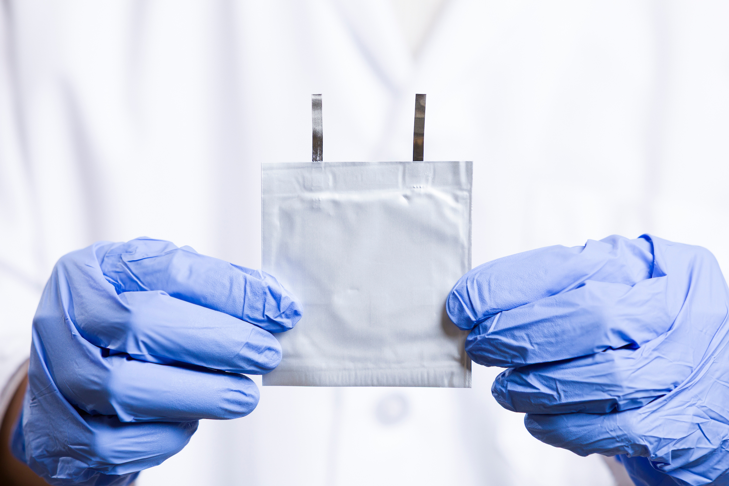 Zwei Hände in blauen Laborhandschuhen halten eine quadratische Batteriezelle