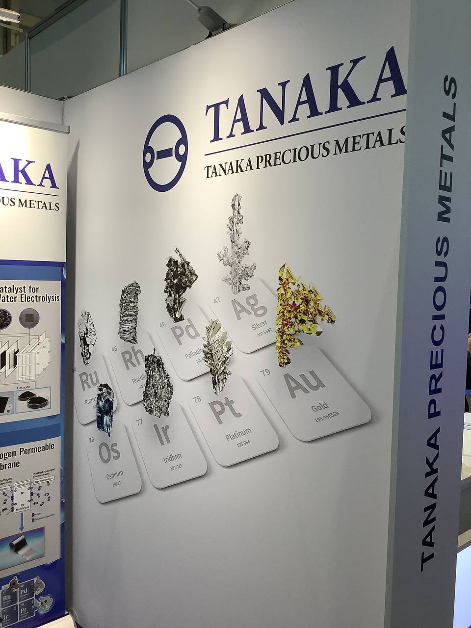 Messewand des Edelmetallkonzerns Tanaka mit Kacheln im Stil des Periodensystems für Ruthenium, Rhodium, Palladium, Silber, Osmium, Iridium, Platin und Gold, jeweils mit einem Foto des Metalls.